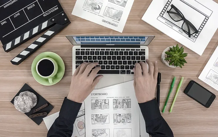 Top view of a creative workspace with a laptop, storyboards, coffee, and design tools